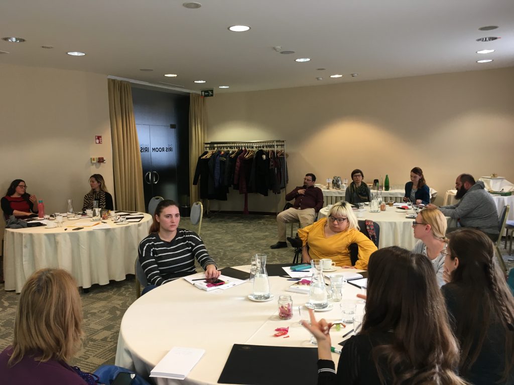 Udeleženci sedijo za tremi okroglimi mizami in razpravljajo o dostopnejših programih za mlade