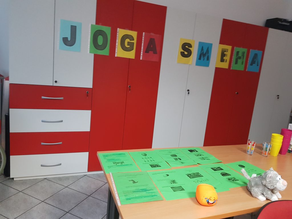 Na društvenih omarah so nalepljeni pisani listi s posameznimi črkami, ki nato sestavijo besedi joga smeha