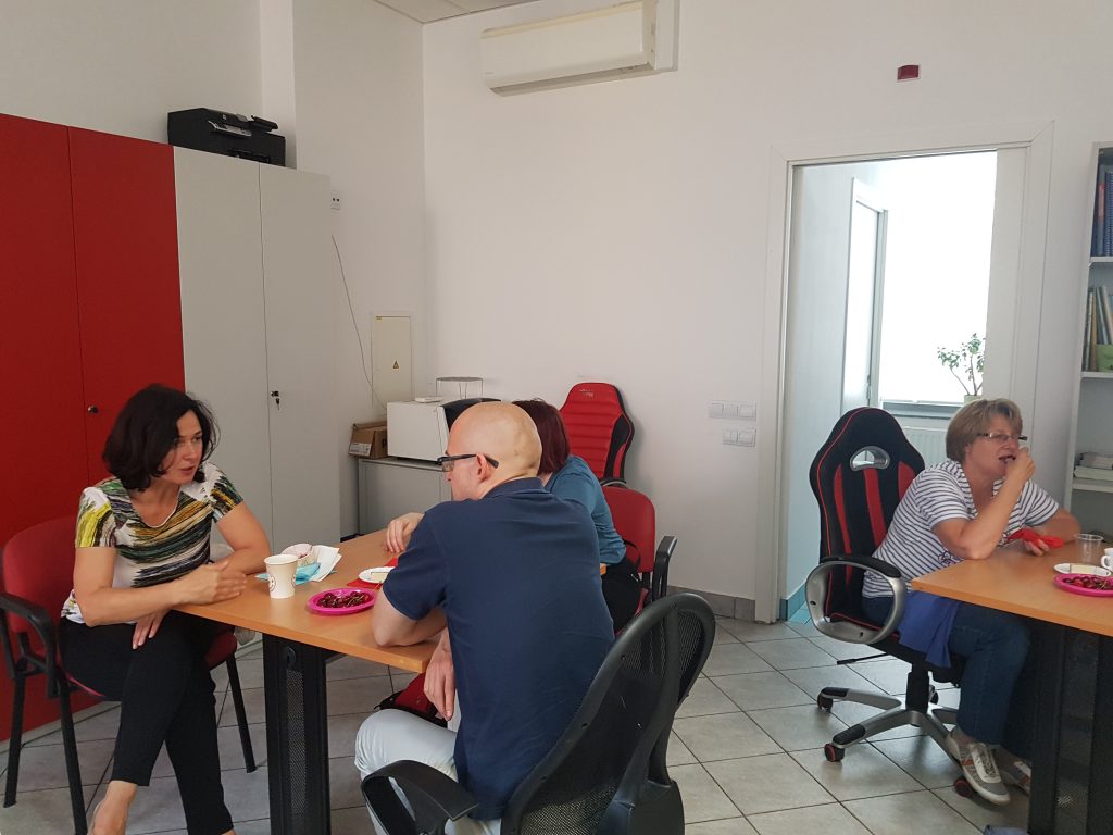 Člani sedijo na stolih ob mizah in klepetajo