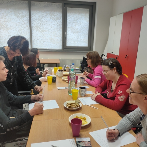 Udeležencu srečanja, ki ima težave z uporabo rok, gostja pomaga pri pisanju