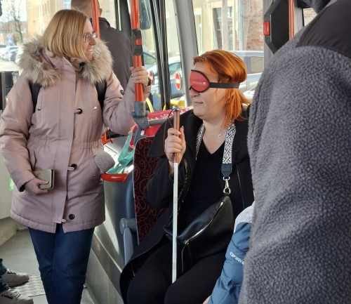 Udeleženka sedi na avtobusu z belo palico in prikritimi očmi