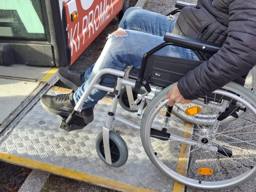 Udeleženec se z invalidskim vozičkom pelje po klančini na avtobus