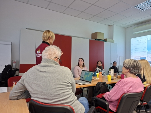 Manja stoji, udeleženci pa sedijo in poslušajo