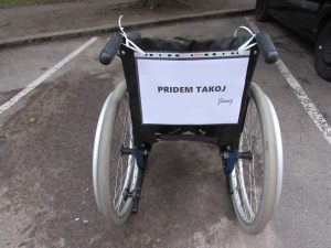 Voziček z napisom pridem takoj, ki opozarja na težave zasedenosti parkirnih mest za invalide