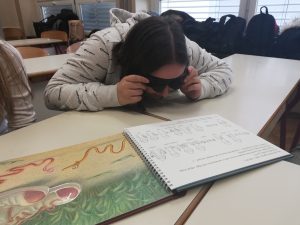 Dijakinja bere slikanico Žiga špaget s simulacijskimi očali