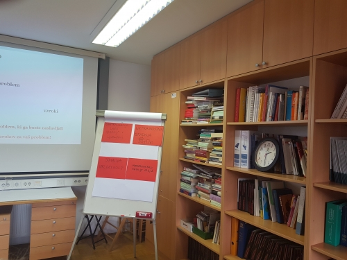 Na beli tabli so prilepljeni štirje A4 rdeči listi s problemom, ki si ga je izbrala posamezna miza udeležencev