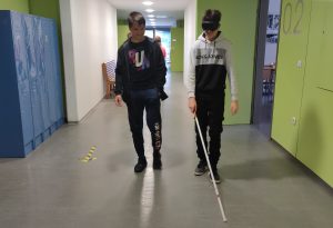 Dijak s črnimi očali hodi z belo palico, drug dijak hodi ob njem