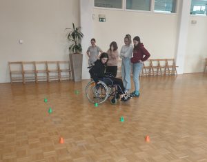 Dijakinja vozi invalidski voziček med stožci