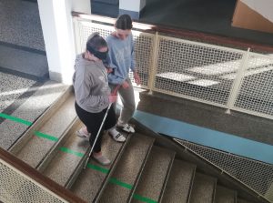 Dijakinja gre z belo palico in spremstvom po stopnicah