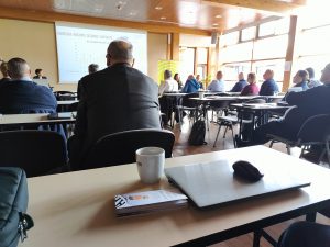 Udeleženci za mizami poslušajo predstavitev Združenja multiple skleroze Slovenije