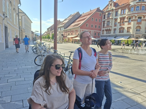 Tri udeleženke na Glavnem trgu nasmejane poslušajo vodiča Jureta
